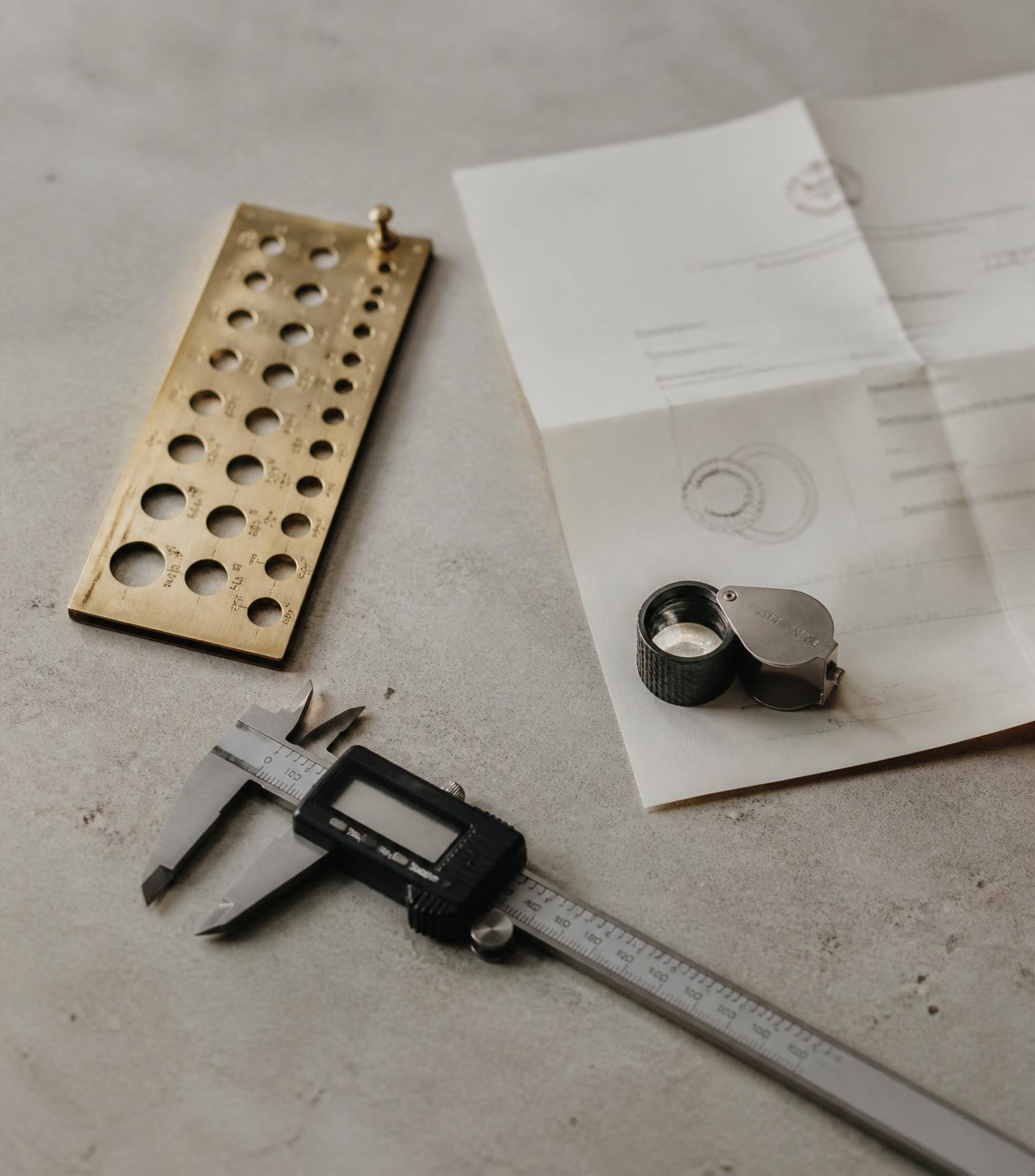 Jeweller's gauge, calipers, loupe and a written valuation document on a stone surface
